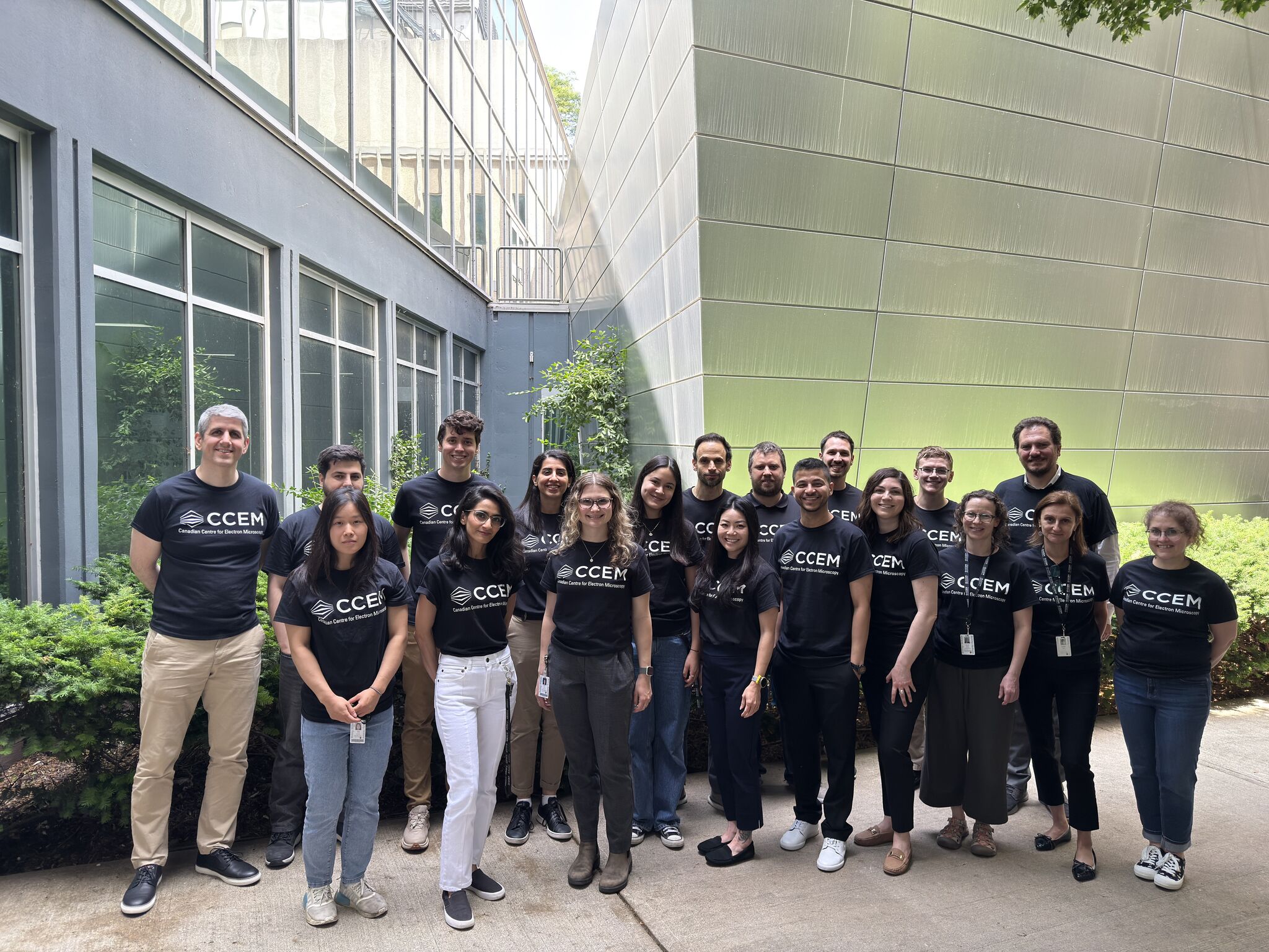 Group of CCEM staff standing in Spectra courtyard smiling at camera, all wearing a black t-shirt with CCEM logo